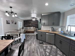 Kitchen featuring gray cabinetry, a sink, wood counters, stainless steel dishwasher, and vaulted ceiling