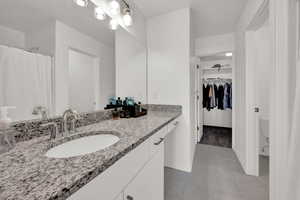 Master Bathroom with tile patterned floors, a walk in closet, toilet, baseboards, and vanity