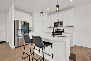 Kitchen featuring stainless steel appliances, light countertops, pendant lighting, a kitchen bar, and light wood-type flooring