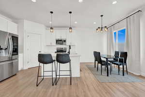 Kitchen featuring light wood finished floors, backsplash, an inviting chandelier, appliances with stainless steel finishes, and light countertops