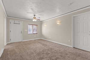 Carpeted empty room featuring ornamental molding, a textured ceiling, and ceiling fan