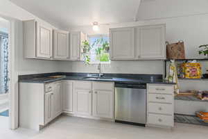 Kitchen featuring stainless steel dishwasher, dark stone counters, light tile patterned floors, and a textured ceiling