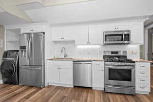 Kitchen featuring light stone countertops, wood finished floors, washer / dryer, a sink, and appliances with stainless steel finishes