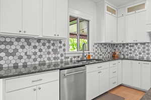 Kitchen with stainless steel dishwasher, dark stone counters, white cabinetry, and a sink