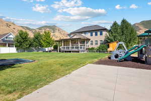 Rear view of house featuring playground community, a yard, a mountain view, and fence