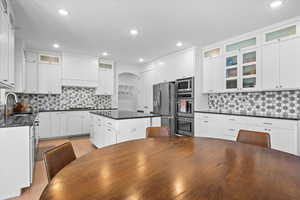 Kitchen with a sink, a center island, white cabinetry, appliances with stainless steel finishes, and glass insert cabinets