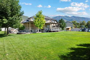 Back of house with a deck with mountain view, a playground, a yard, and fence