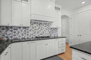 Kitchen featuring light wood-type flooring, custom range hood, arched walkways, white cabinets, and stainless steel gas cooktop