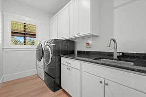 Washroom featuring a sink, washing machine and dryer, cabinet space, light wood finished floors, and baseboards