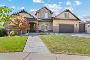 Craftsman house featuring stone siding, stucco siding, an attached garage, and a front lawn