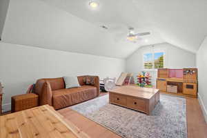 Living room featuring ceiling fan, vaulted ceiling, visible vents, and light wood-type flooring