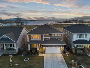 View of front facade with roof with shingles, a lawn, stone siding, driveway, and a water and mountain view