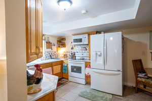 Kitchen with open shelves, backsplash, white appliances, light countertops, and light tile patterned floors