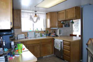 Kitchen with brown cabinets, stainless steel dishwasher, light countertops, and a sink