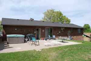 Rear view of property featuring a patio, brick siding, a yard, a hot tub, and a chimney