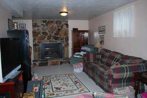 Living area with a textured ceiling, a stone fireplace, and carpet flooring