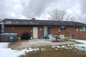 Snow covered property featuring a chimney, a patio area, brick siding, and a hot tub