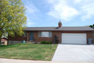 Ranch-style house featuring a chimney, brick siding, a garage, a front lawn, and concrete driveway