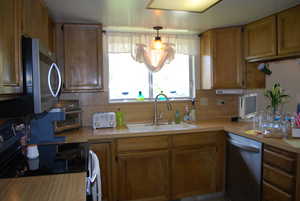 Kitchen featuring a sink, stainless steel appliances, light countertops, brown cabinetry, and backsplash
