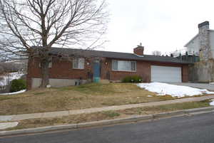 Ranch-style house featuring an attached garage, a chimney, a front lawn, concrete driveway, and brick siding