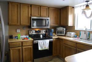 Kitchen featuring brown cabinets, appliances with stainless steel finishes, light countertops, and a sink