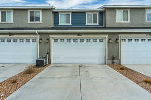 View of front of house with central AC unit, stucco siding, concrete driveway, and a garage