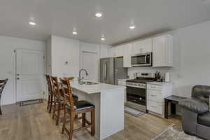 Kitchen with a breakfast bar area, light wood-type flooring, appliances with stainless steel finishes, white cabinets, and a sink