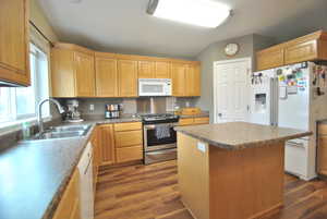 Kitchen with a sink, white appliances, stainless steal gas stove a kitchen island, and wood style finished floors