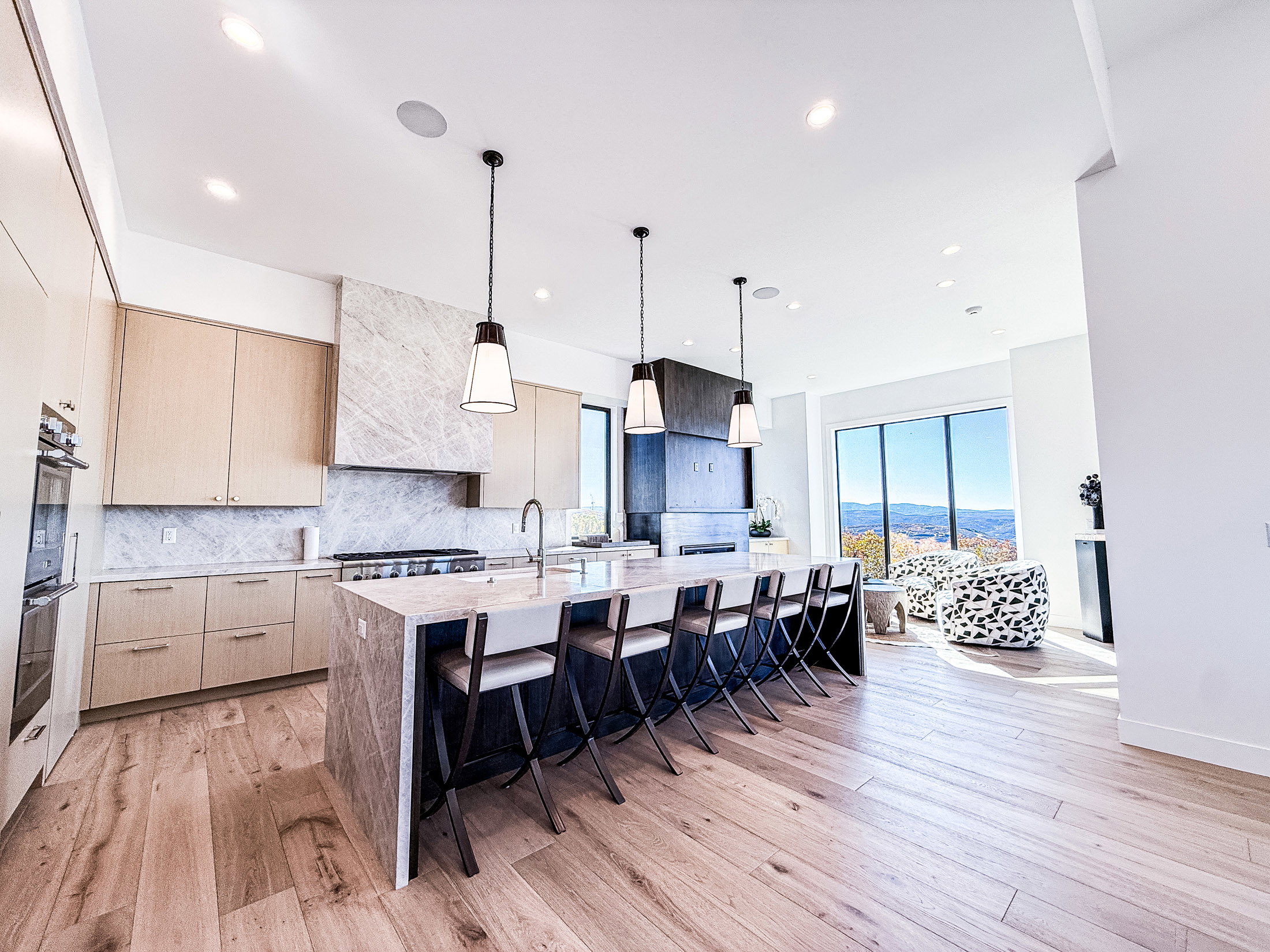 Kitchen with light stone counters, backsplash, a large island, a kitchen bar, and light brown cabinetry