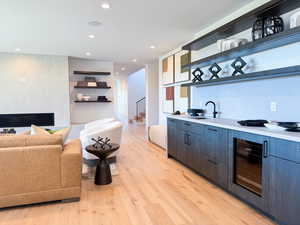 Bar area with open shelves, a large fireplace, modern cabinets, light countertops, and light wood-type flooring