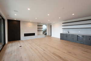 Unfurnished living room with a fireplace, indoor wet bar, stairway, recessed lighting, and light wood-style flooring