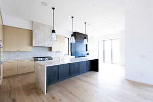 Kitchen with stainless steel gas cooktop, a kitchen island with sink, modern cabinets, light wood-style flooring, and backsplash
