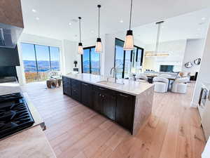 Kitchen with open floor plan, decorative light fixtures, light stone counters, light wood-style flooring, and a center island with sink