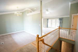 Interior space with baseboards, lofted ceiling, ornamental molding, carpet flooring, and ceiling fan with notable chandelier