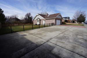 View of home's exterior featuring brick siding, fence, concrete driveway, a chimney, and a garage