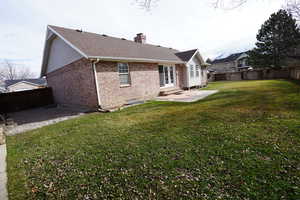 Back of property featuring brick siding, entry steps, a chimney, a yard, and a fenced backyard