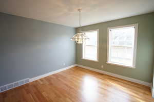 Unfurnished room featuring a notable chandelier, visible vents, light wood-style floors, and baseboards