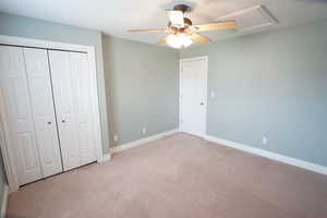 Unfurnished bedroom featuring a ceiling fan, baseboards, attic access, a closet, and light carpet