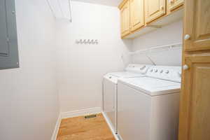Clothes washing area featuring light wood-style flooring, electric panel, cabinet space, separate washer and dryer, and baseboards