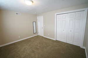 Unfurnished bedroom featuring visible vents, a textured ceiling, a closet, carpet flooring, and baseboards