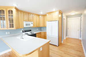 Kitchen featuring white appliances, light countertops, a peninsula, and light brown cabinetry