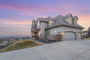 View of front of home with a front yard, roof with shingles, driveway, stucco siding, and stone siding