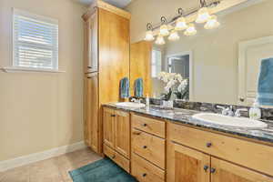 Bathroom featuring tile patterned flooring, double vanity, baseboards, and a sink