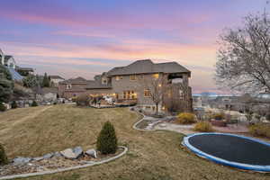 Back of house at dusk with an outdoor living space with a fire pit, a trampoline, roof with shingles, a lawn, and a deck