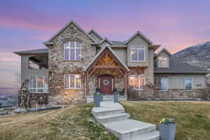 View of front of property with a balcony, stone siding, stucco siding, and a yard