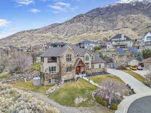 View of front of house featuring stone siding, concrete driveway, a balcony, and a shingled roof