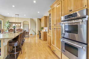 Kitchen featuring light wood finished floors, double oven, a breakfast bar area, recessed lighting, and arched walkways