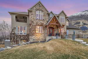 View of front facade with a lawn, stucco siding, a balcony, stone siding, and a mountain view
