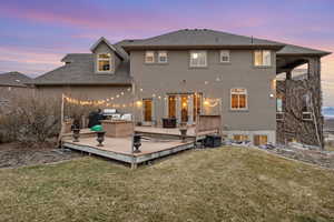 Back of house at dusk with stucco siding, a lawn, roof with shingles, and a wooden deck