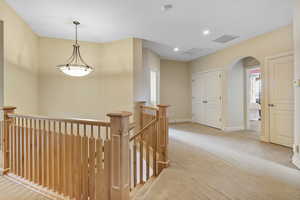 Hallway featuring visible vents, an upstairs landing, arched walkways, carpet flooring, and baseboards